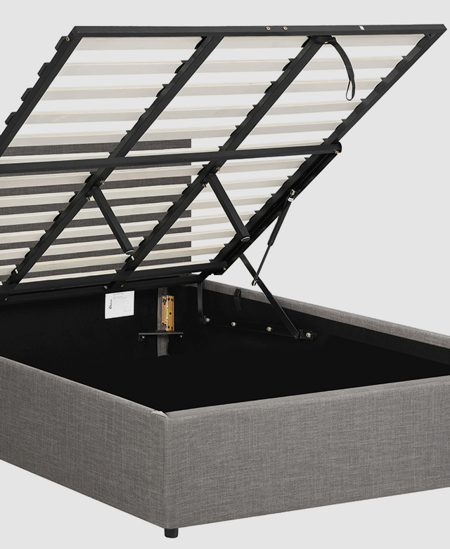 The slatted mattress support of the grey bed is elevated to reveal storage space beneath.