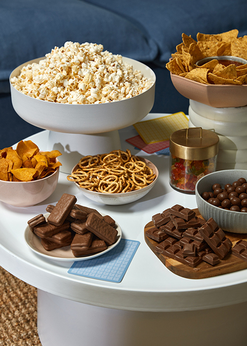 Bowls of snacks, including popcorn, chips and chocolate, sitting on top of a round coffee table