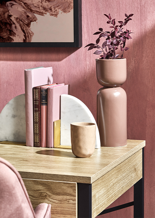 A close up of two marble half arch bookends with gold stands at either end of 1four blush coloured books on a wooden desk with a blush coloured ceramic vase
