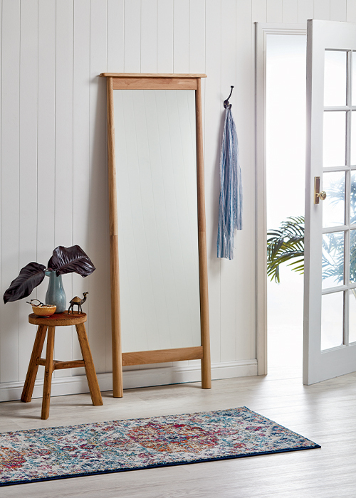 A coastal styled entryway with a rectangular wood framed leaner mirror by the front door