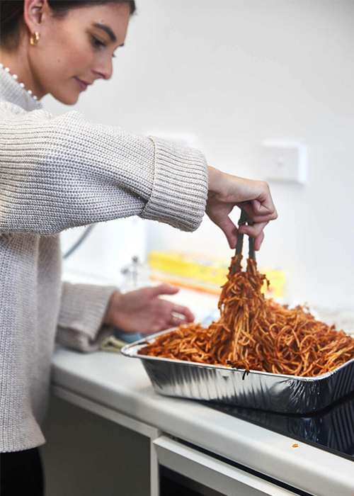 A women serving spaghetti bolognese from a large tray using tongs 