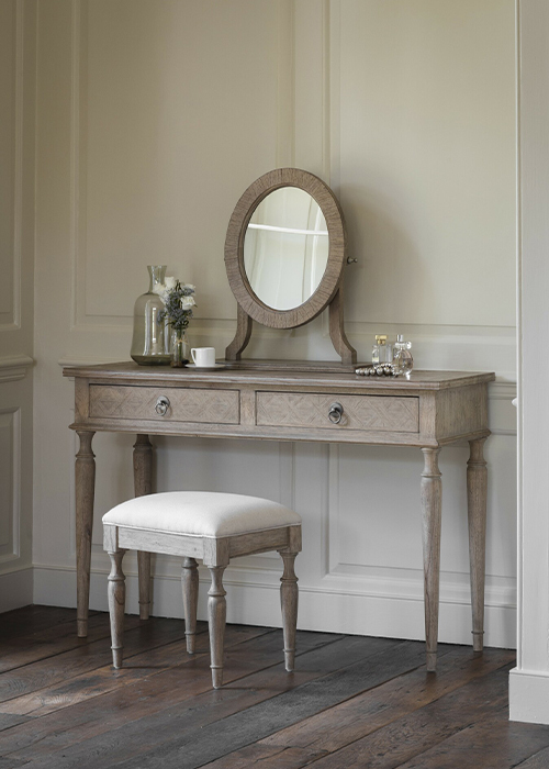 A vintage style cream dressing table with ornate legs and a wood and upholstered stool