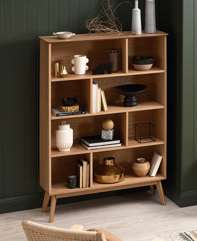 The bookshelf is styled in front of a dark green panelled wall, with every shelf filled with decor and books. The bookshelf is styled in front of a dark green panelled wall, with every shelf filled with decor and books.