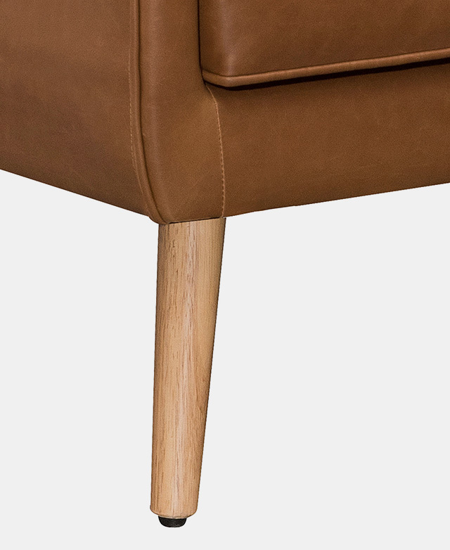 A smooth wooden leg underneath a tan chair features a tapering shape and a black foot pad at the tip.