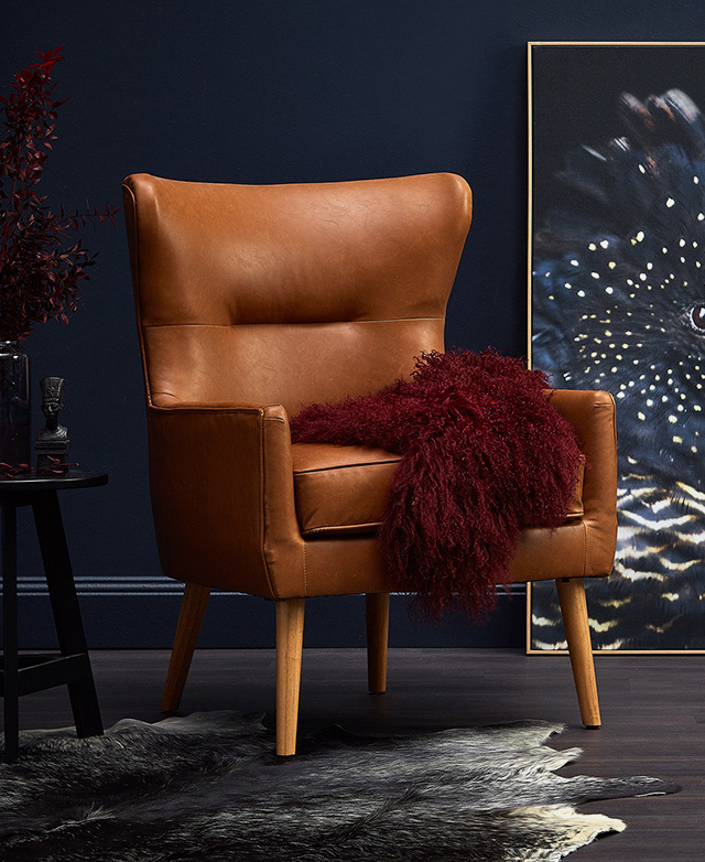 A tan faux leather armchair with timber legs has a shaggy red throw draped over the seat.