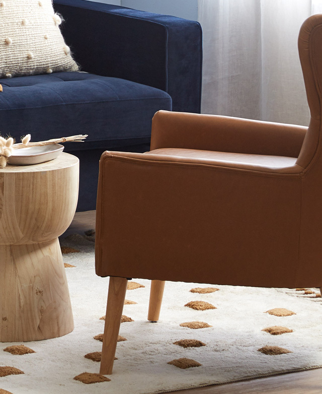 Above a soft, bohemian-inspired rug, a tan faux leather accent armchair is positioned in front of a timber side table.