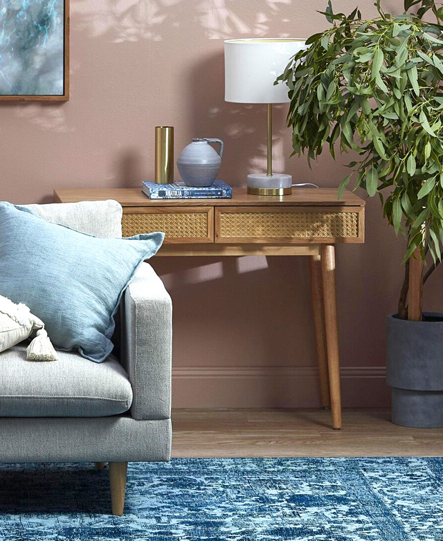 In situ in a coastal-inspired living room, a timber console table is styled behind a sofa and next to a leafy green plant.