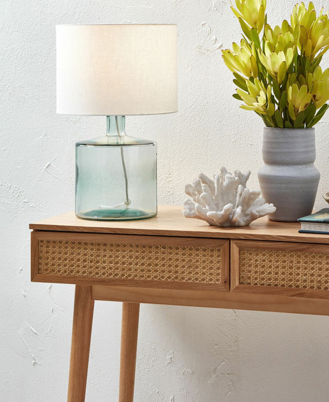 Close-up of the rattan drawers on the console table, flush against a textured white wall with coastal-themed decor on top.