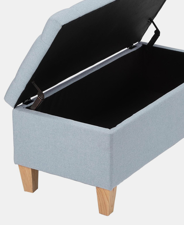 Three-quarter angle of an ottoman with blue upholstery and timber legs. The top is lifted, revealing storage space within. Three-quarter angle of an ottoman with blue upholstery and timber legs. The top is lifted, revealing storage space within.