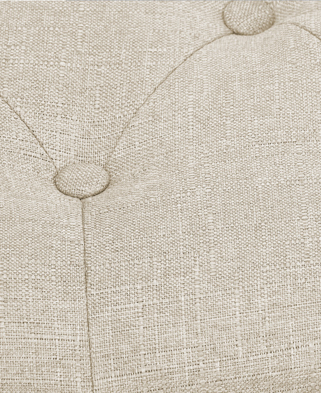 Extreme close-up of the foam-padded and button-tufted polyester top of the ottoman. The upholstery is in a beige colour.