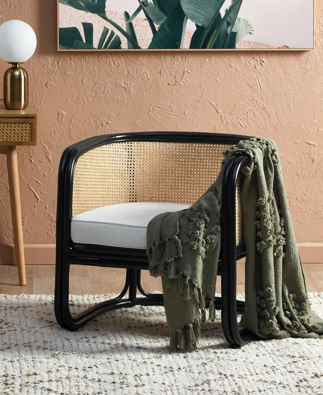 A black-framed rattan armchair that's draped with an olive throw is positioned on top of the rug.