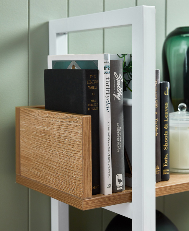 A close crop highlights the angular metal frame and the wood grain of the end of a particleboard shelf. Books fill it. A close crop highlights the angular metal frame and the wood grain of the end of a particleboard shelf. Books fill it.