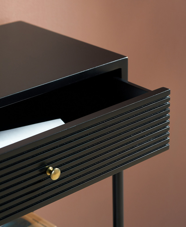 The grooved front of an open drawer is displayed up close. It has one polished brass knob.