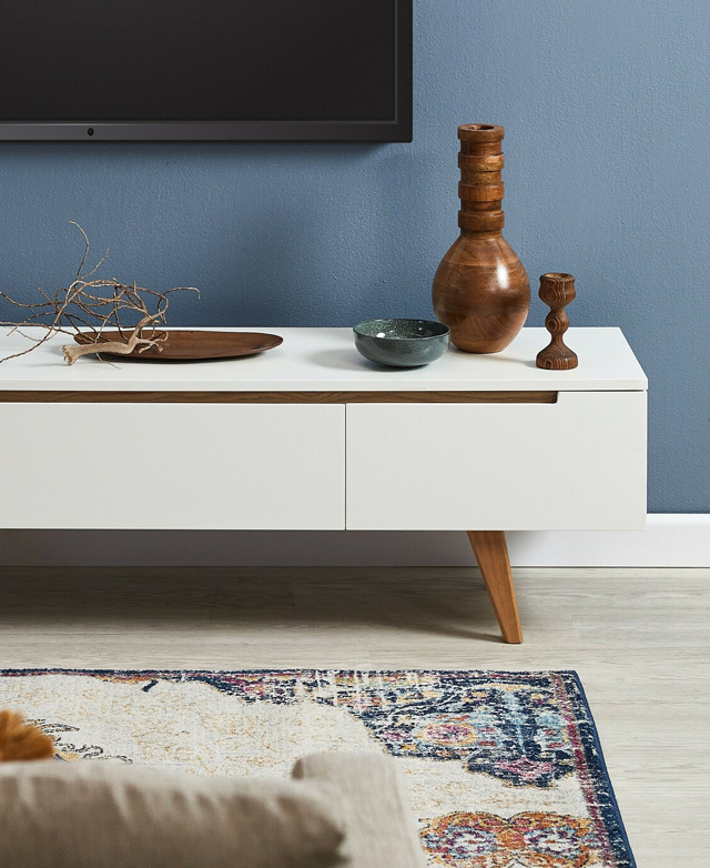 The TV unit is styled in front of a blue wall. It has wooden accents on top, and a TV is hung on the wall over it.