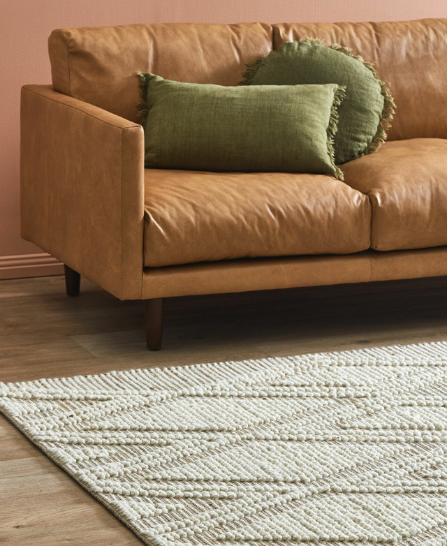 Appearing from an angle, the rug is styled in front of a tan leather sofa, which has two soft green cushions on top.