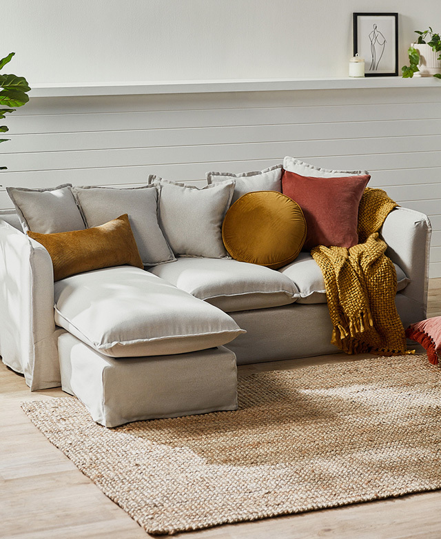 Situated in front of a white, panelled wall and next to a jute rug, the soft-toned sofa is topped with rich, cosy cushions.