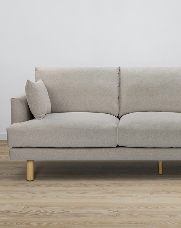 Eye-level view of a three-seater sofa upholstered in smooth grey fabric. Cylindrical rubberwood legs lift it off the floor. Eye-level view of a three-seater sofa upholstered in smooth grey fabric. Cylindrical rubberwood legs lift it off the floor.