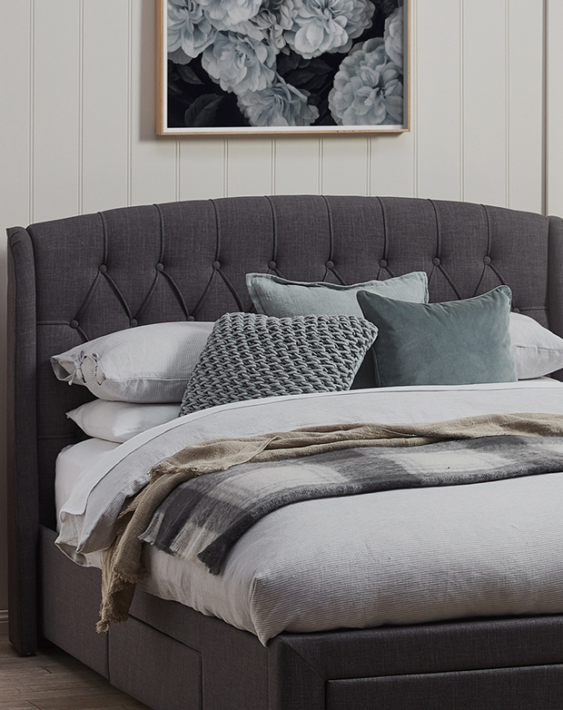 Smooth, gently arched bedhead is enhanced with the pile of soft blue cushions in front of it.