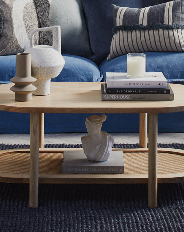 Side view of a double shelf coffee table. A wooden frame consisting of four pillar legs connect the two stacked oval shelves.