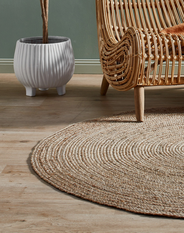 The rug is on a timber floor, with a rattan armchair positioned on the edge.