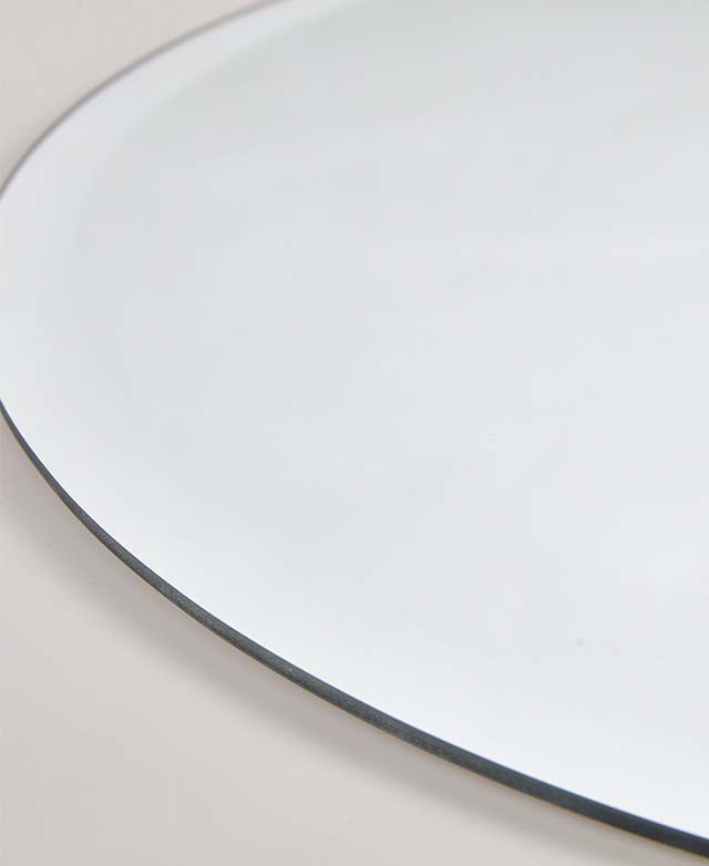 Close-up of round frameless wall mirror, thin polished edge detail against a light wall.