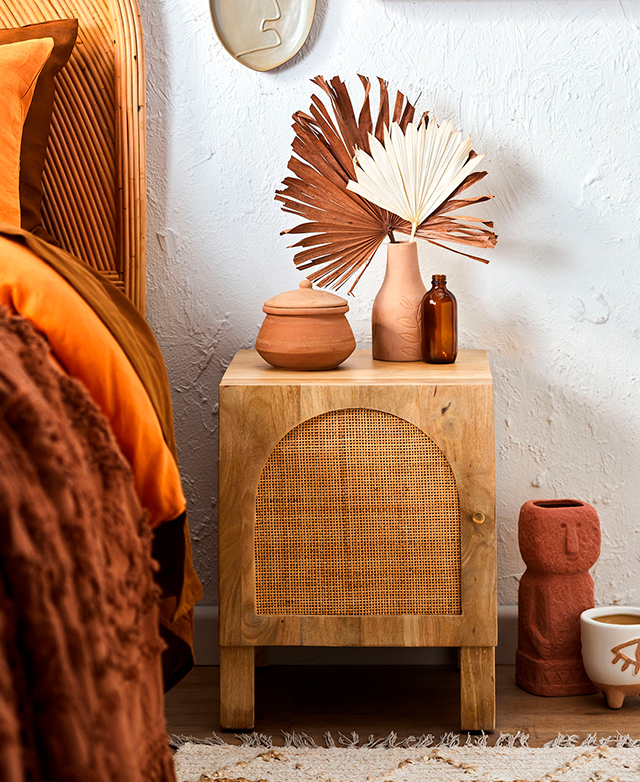 A mango wood and rattan bedside table in an earthy bedroom space full of vibrant orange hues.