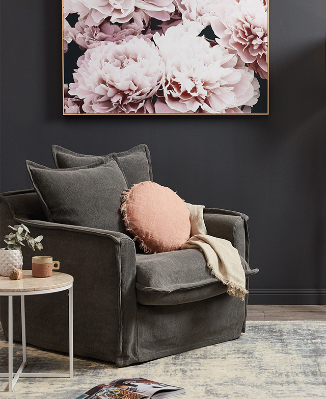 A blockish armchair in situ, positioned underneath hanging floral artwork and above a distressed area rug. A blockish armchair in situ, positioned underneath hanging floral artwork and above a distressed area rug.