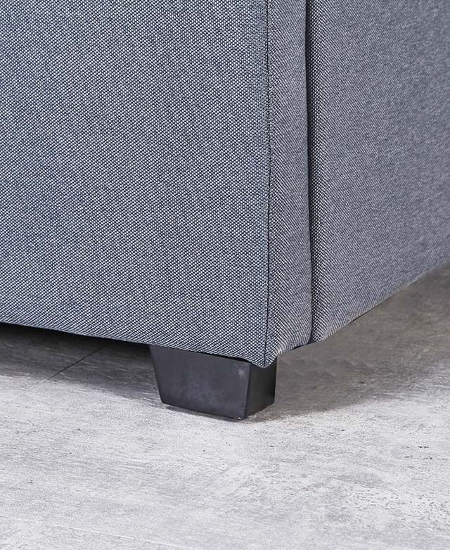The close-up image depicts a bottom corner of the upholstered bed, and a short black foot.