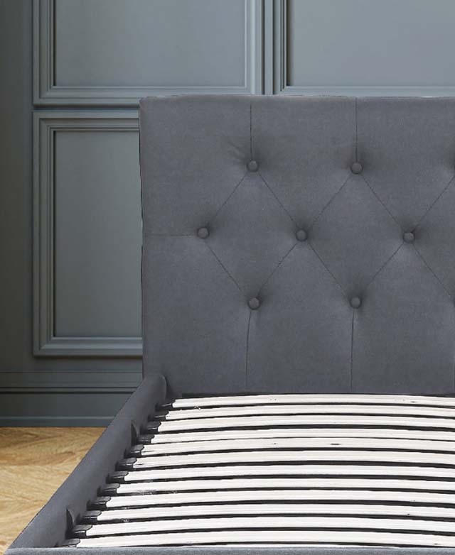 The bed frame is in front of a blue-grey panelled wall. The button tufted headboard is centre stage.