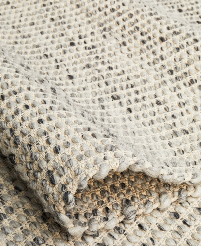 Folded over and close-up, the details of the rug's salt and pepper woven wool is displayed.