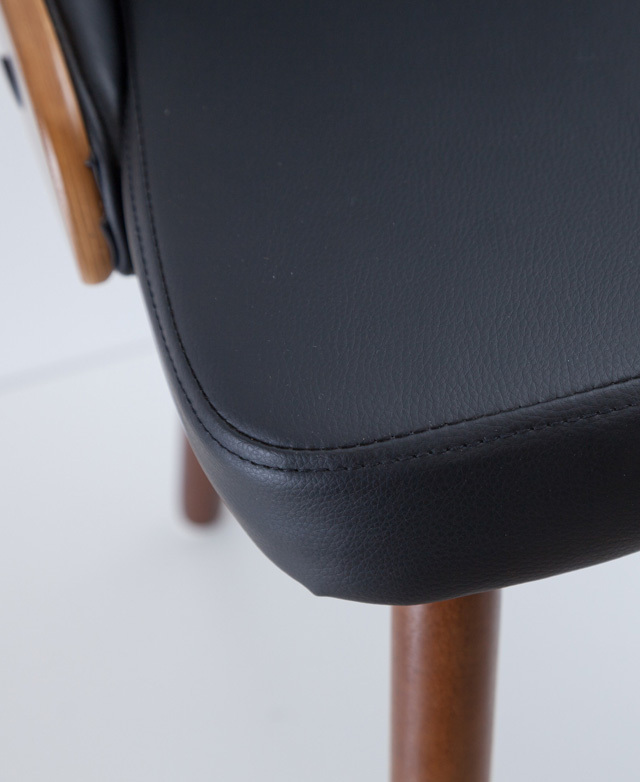 Close up of the stitch detail on the corner of a dining chair seat cushion. It has black faux leather upholstery.