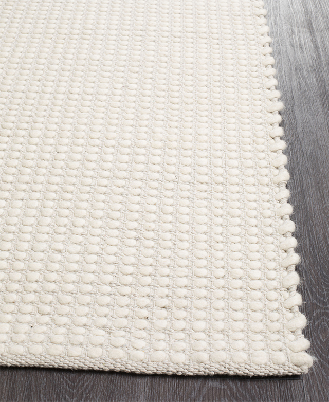 A white wool and cotton rug with a high-low pile is positioned on top of dark timber flooring.