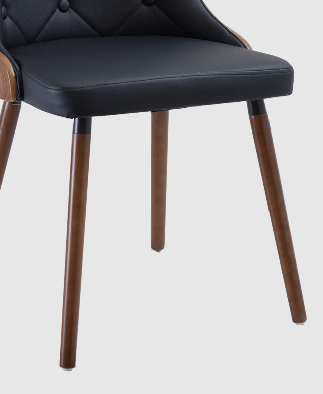 Timber legs underneath a faux leather dining chair with a mid-century aesthetic.