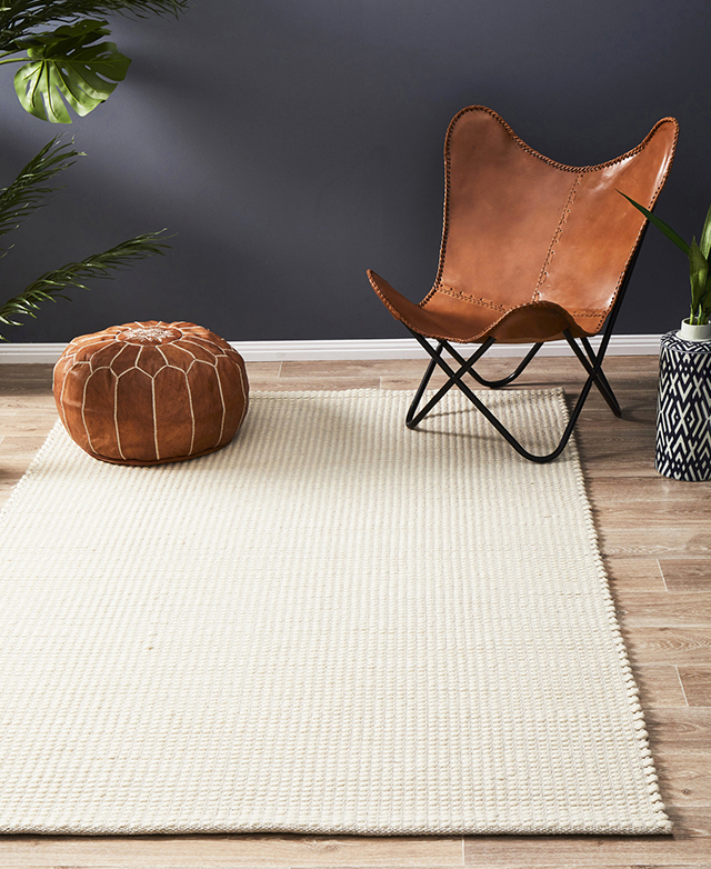 A white wool area rug is styled in a casual space, along with a tan leather butterfly chair and moroccan-style ottoman.