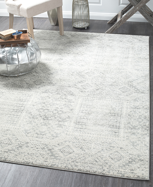 The rug is styled on top of dark timber flooring, enhancing its grey and silver tones.