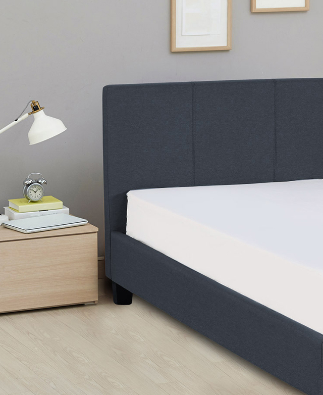 The bed is assembled and features a mattress fitted with a white sheet. A simple side table is next to it. The bed is assembled and features a mattress fitted with a white sheet. A simple side table is next to it.