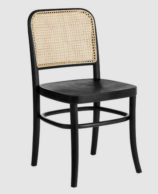 The black variant of the chair is shown from the front at a slight angle. The smooth edges and rattan backrest are depicted. The black variant of the chair is shown from the front at a slight angle. The smooth edges and rattan backrest are depicted.