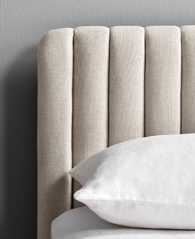 The close-up image exhibits the linen-like texture of the fabric that upholsters the bedhead.