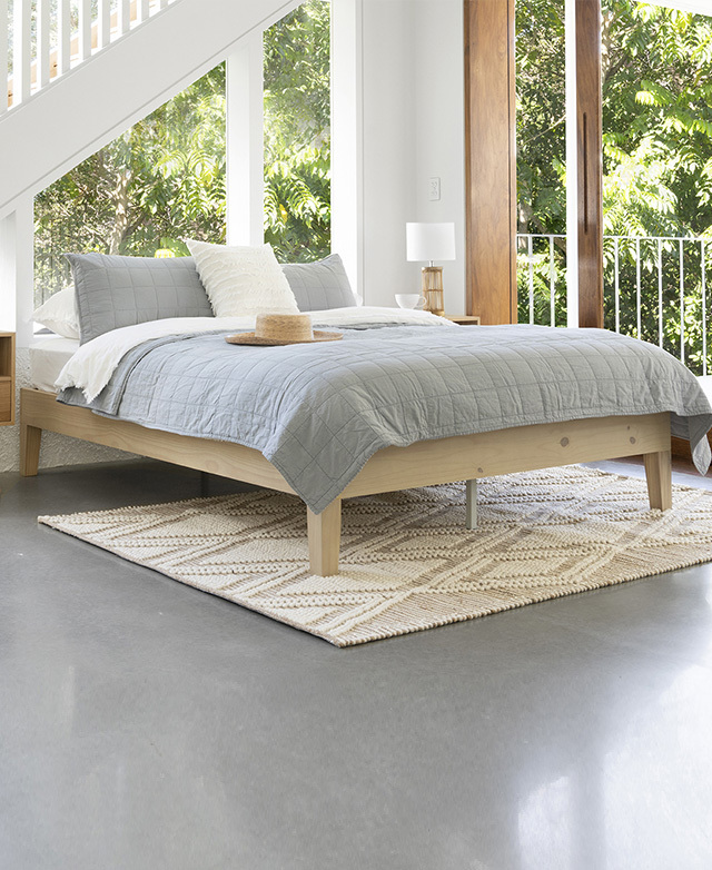 The whitewash base is displayed from a front angle beneath a light grey, grid-patterned coverlet and white bedding.