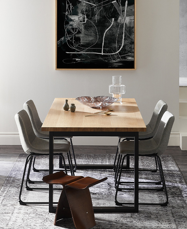A butterfly stool and four grey, sleigh leg chairs are drawn to the table, which has a glass bowl and other accents on top.