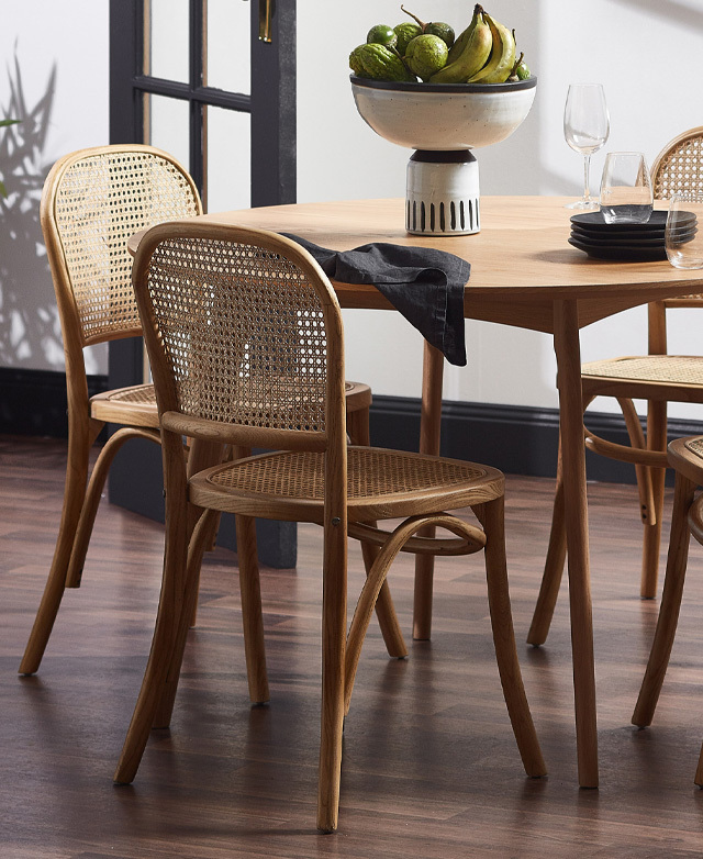 A back angle of the chair in situ at a dining table, showing the bentwood frame and open weave rattan backrest and seat.