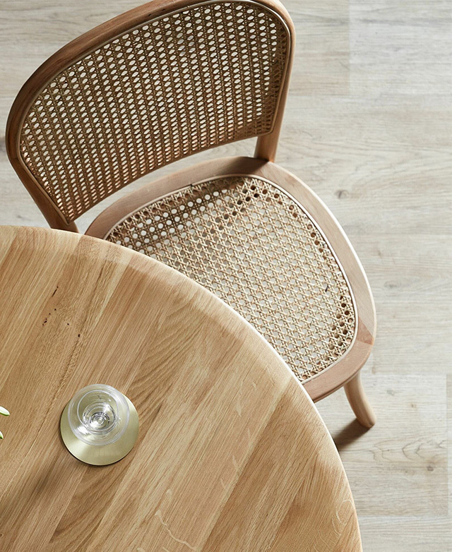 A bird's eye snapshot that shows a chair partially tucked beneath a table, with rattan weave on display.