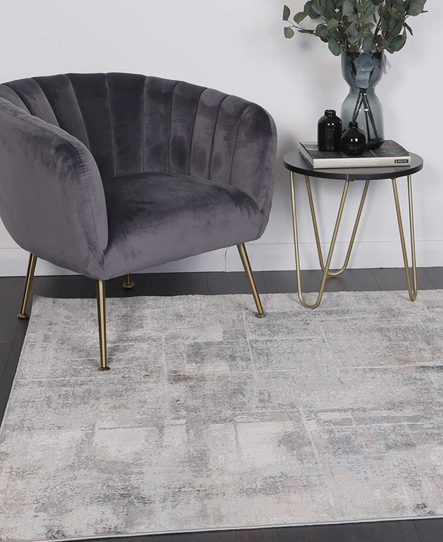 The beige and grey rug is styled on top of dark timber flooring and underneath a contemporary accent chair and side table.