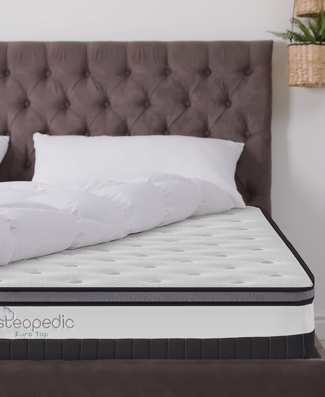 The mattress is fitted onto an upholstered bed frame with a white quilt turned back on top.