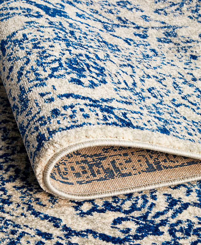 A blue and white rug folded over, illustrating the 10mm pile, jute warp and weft backing, and serged edge.