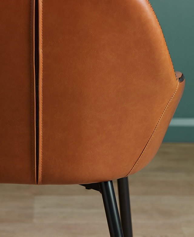 The back of the chair is shown. It has black powder-coated metal legs splayed out from under the base of the seat. The back of the chair is shown. It has black powder-coated metal legs splayed out from under the base of the seat.