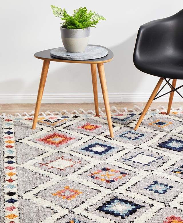 A rug with a colourful, geometric pattern and fringe trim is styled underneath the legs of surrounding furniture.