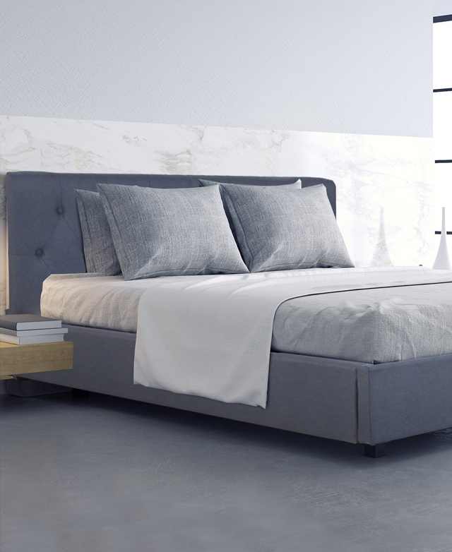 The bed is fully assembled and dressed in shades of grey. It's on a light grey floor, and in front of a white marbled wall.