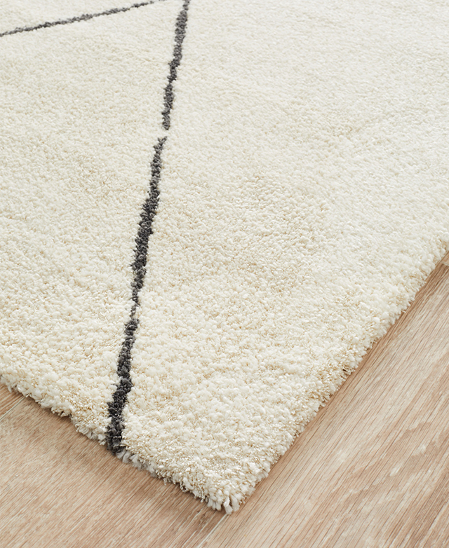 Corner of a cream-toned rug on top of timber flooring, highlighting the soft texture of its 1.4cm pile height. Corner of a cream-toned rug on top of timber flooring, highlighting the soft texture of its 1.4cm pile height.
