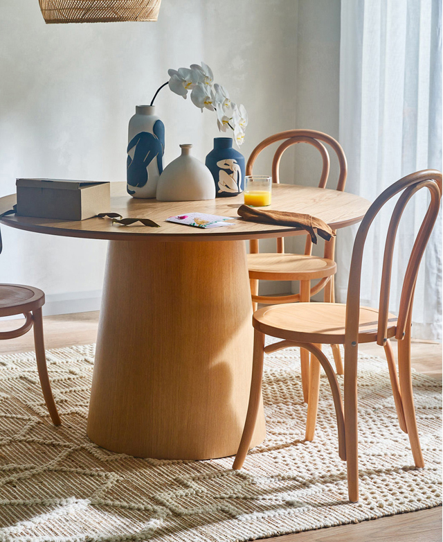 The chairs are positioned around a pedestal table in a warmly lit breakfast room. Ceramics and an orchid are in the centre.